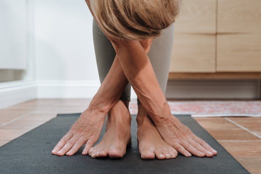 Senior adult woman practicing a forward bend asana on a yoga mat indoors, promoting flexibility and wellness.
