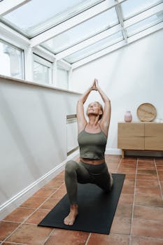 Elderly woman doing yoga pose on mat indoors with arms raised.