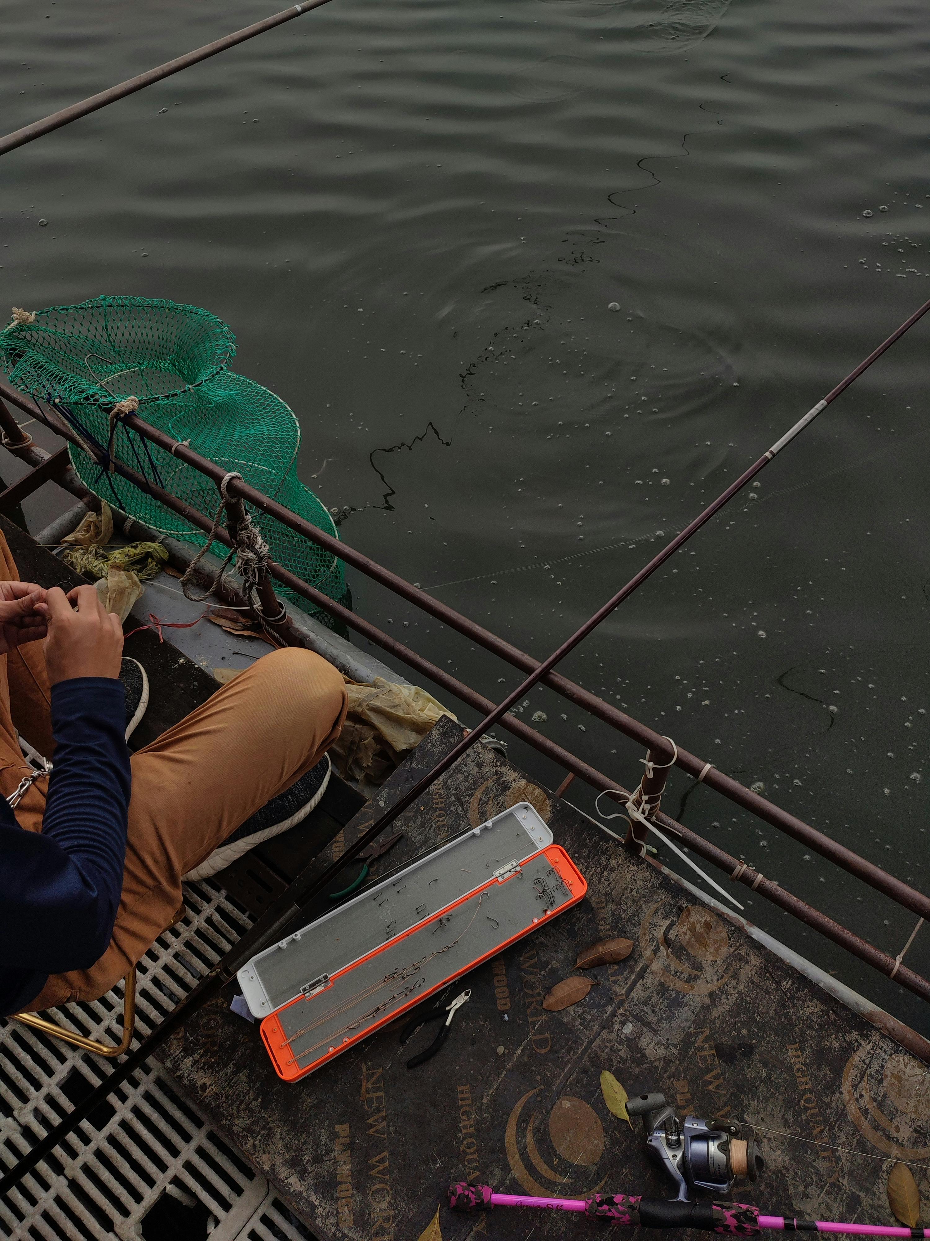 A man fishing from a boat in Trảng Bom, Dong Nai, Vietnam, using a rod and net.