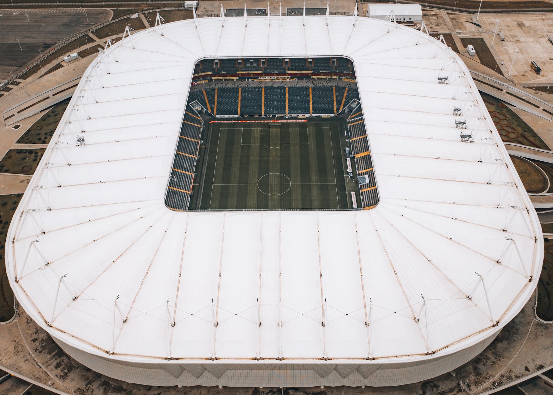 High-angle aerial shot of a modern stadium with a white roof and green field inside.
