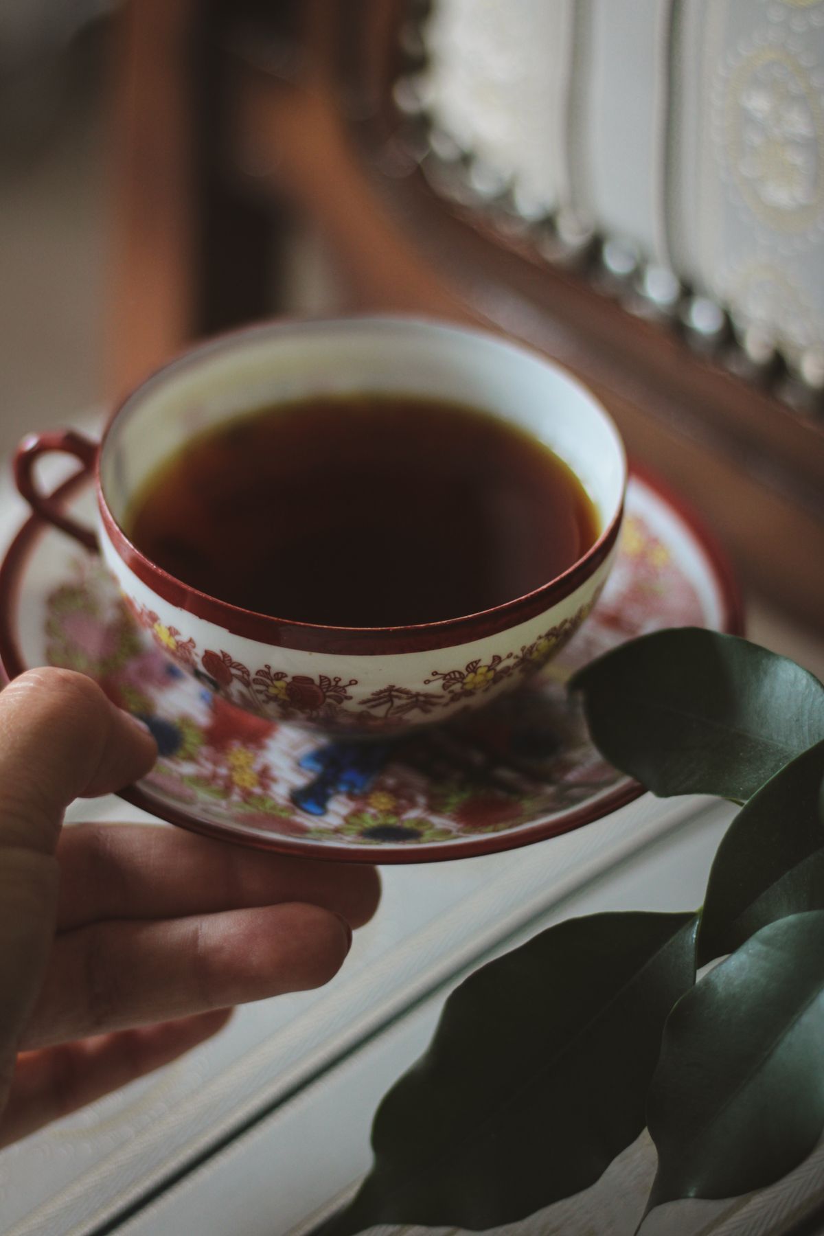 An elegant ceramic teacup beside fresh plant leaves