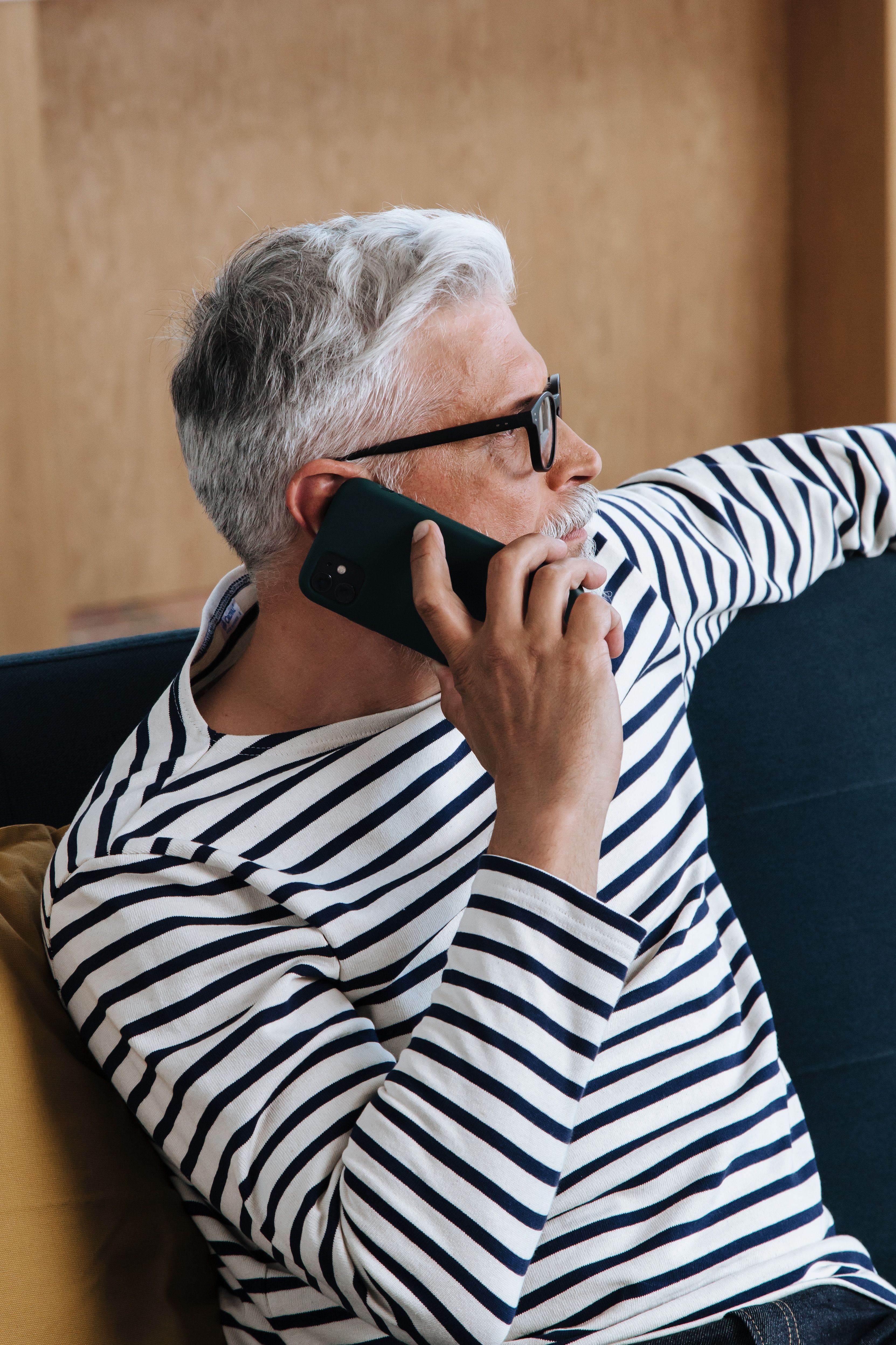 A senior man with grey hair using a smartphone while relaxing at home.