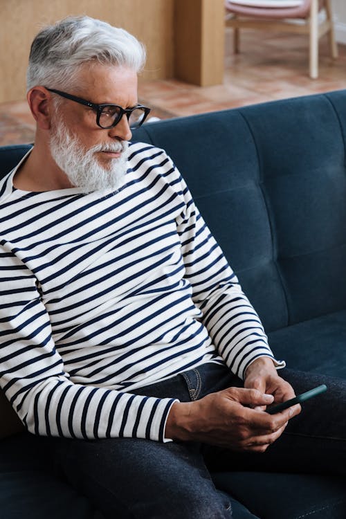 Free Man Sitting on Couch and Looking at Phone Stock Photo