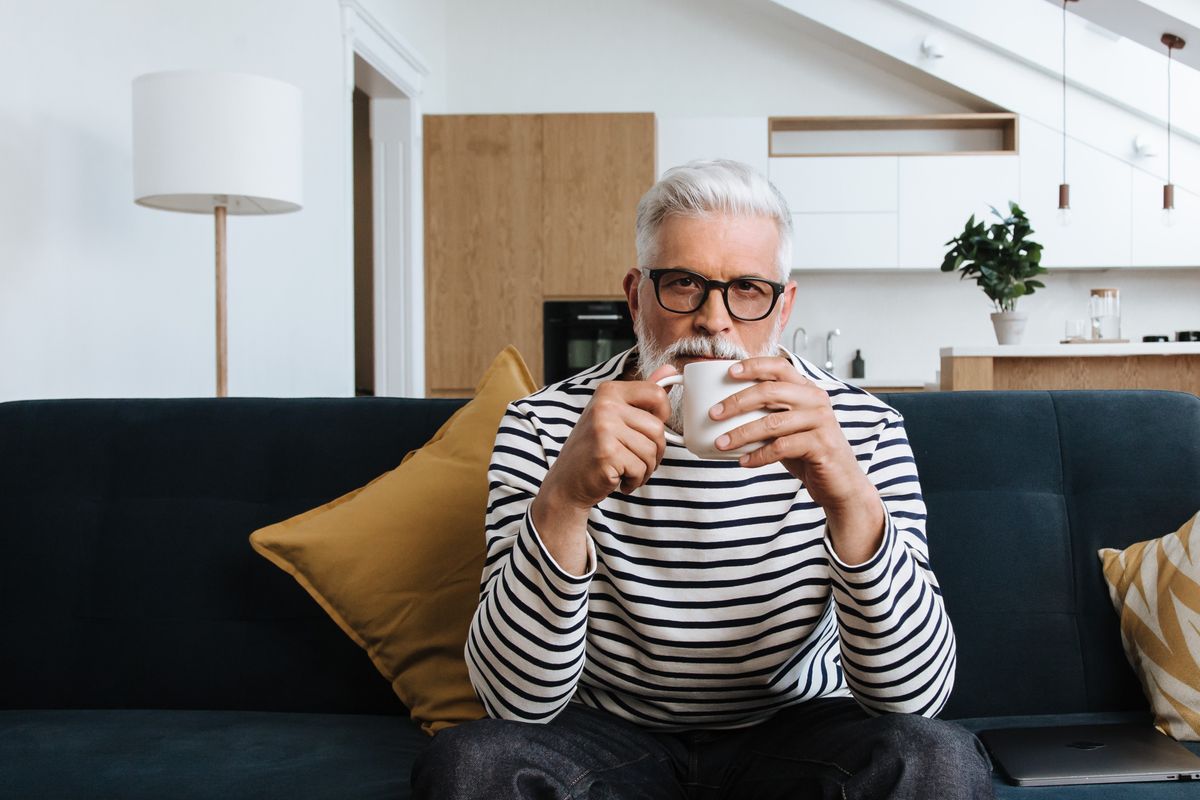 Hombre mayor relajado tomando café en su living, sin gráficos ni pantallas cerca