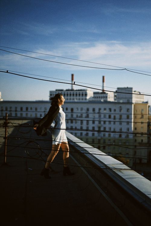 Free A woman stands on a rooftop with arms outstretched, surrounded by city buildings and blue sky. Stock Photo