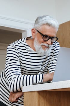 Elderly man with grey hair focuses on his laptop, working from home.