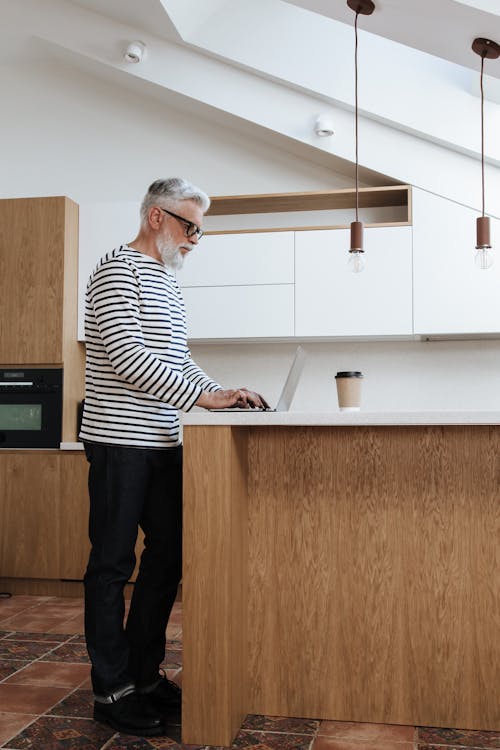 Free A Side View of a Senior Male Adult Standing and Typing on a Laptop  Stock Photo