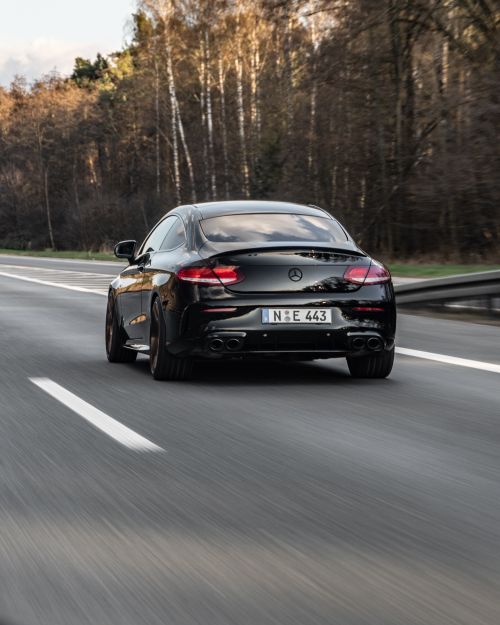 Free A sleek black car driving on the highway surrounded by trees, showcasing luxury travel in Germany. Stock Photo