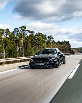 Sleek black Mercedes-Benz sedan driving on a highway in Nürnberg, Germany, surrounded by forests.