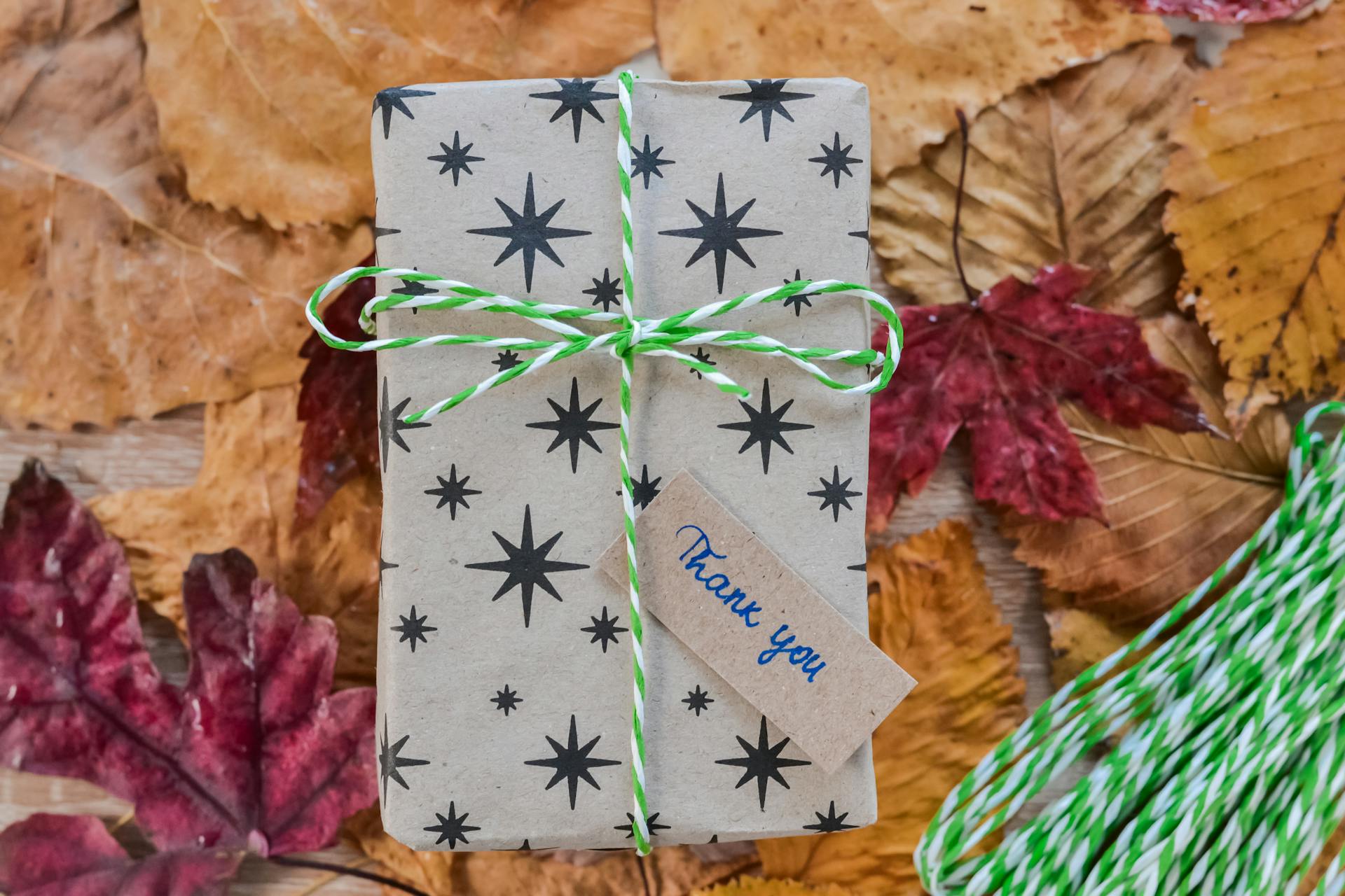Decorative gift box with thank you note, wrapped in starry paper, on autumn leaves.