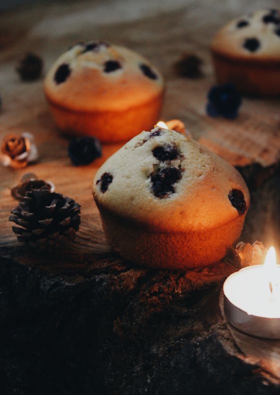 Pale golden blueberry muffins on a rustic wood slice with pine cones and a candle