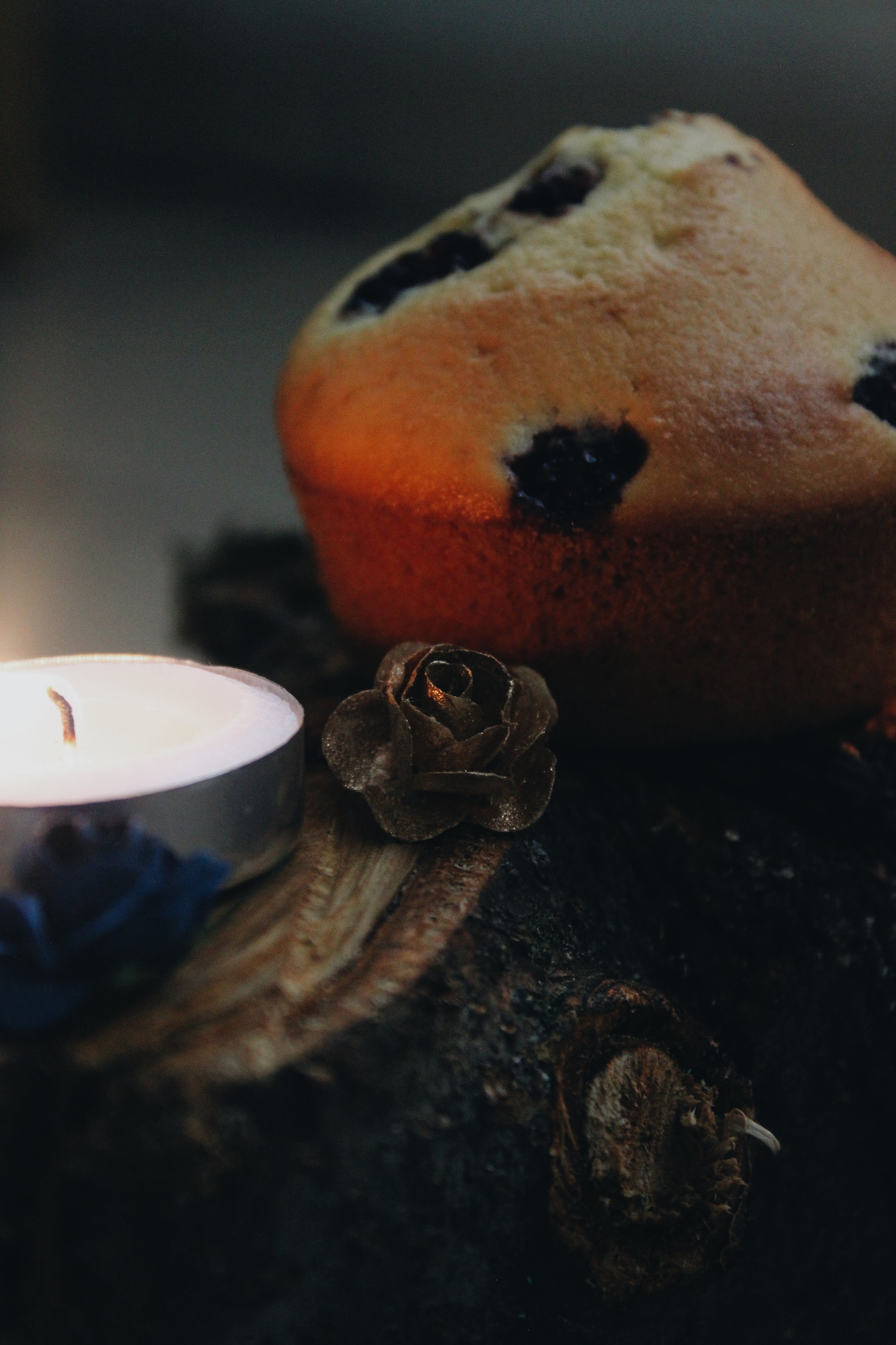 A warm muffin beside a candle on a rustic wooden surface, creating a cozy ambiance.