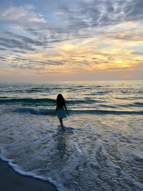 Free A woman walks along a peaceful beach during a stunning sunset, with waves gently lapping at her feet. Stock Photo