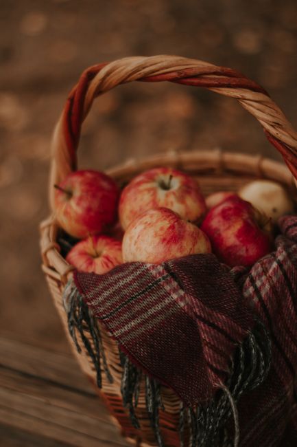 A warm autumnal scene featuring red apples in a wicker basket adorned with a cozy scarf.