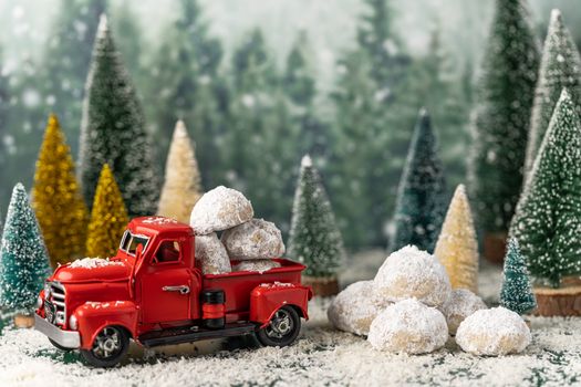 Red vintage toy truck carrying snowball cookies in a snowy Christmas forest setting.