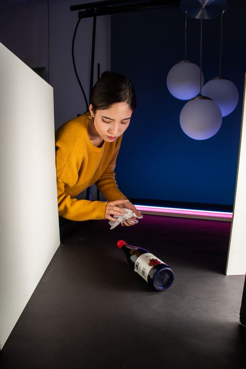 Free Woman arranging a wine bottle in a modern studio setup with stylish lighting. Stock Photo