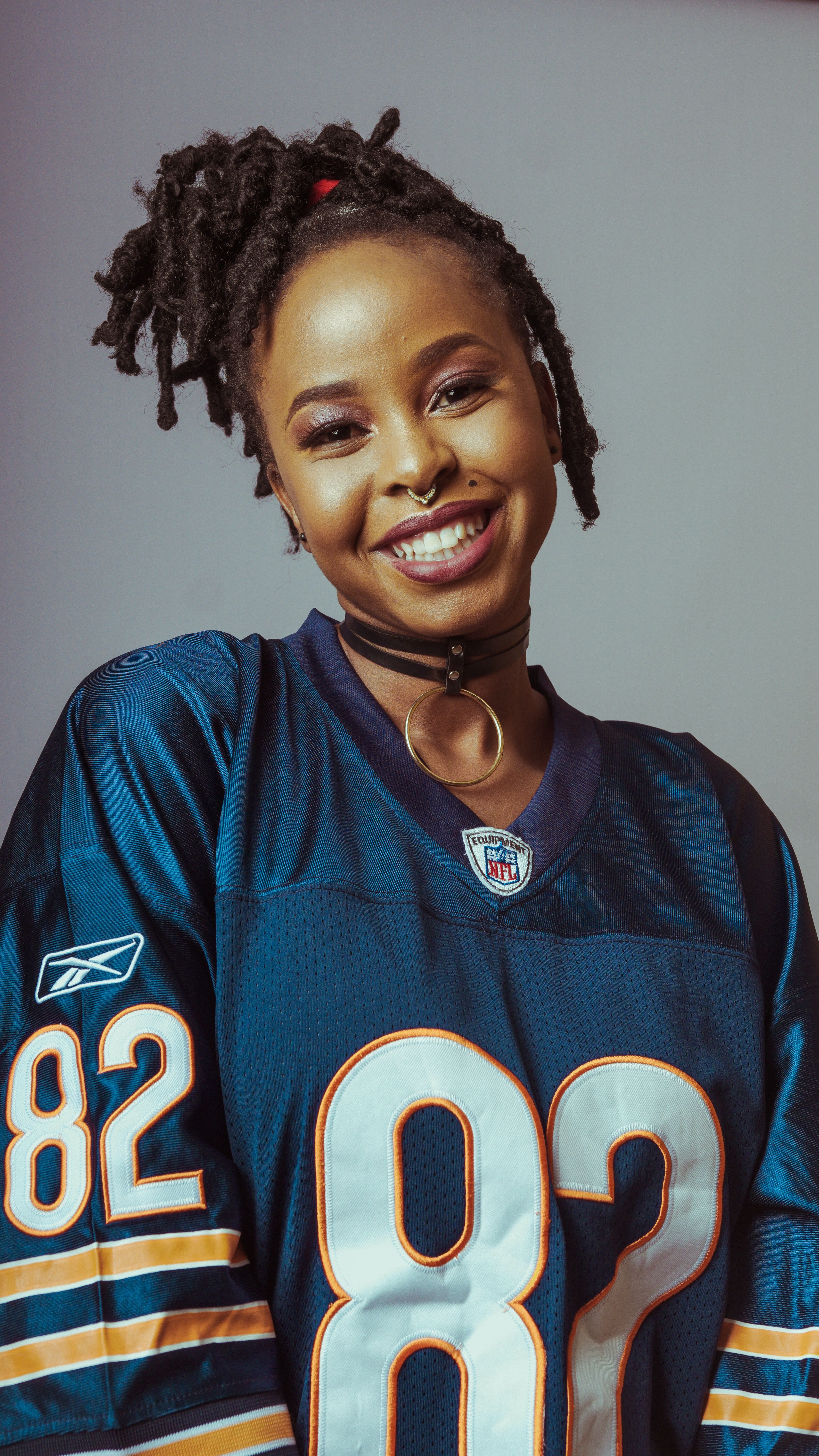Smiling woman in an oversized blue jersey, captured in a studio setting.