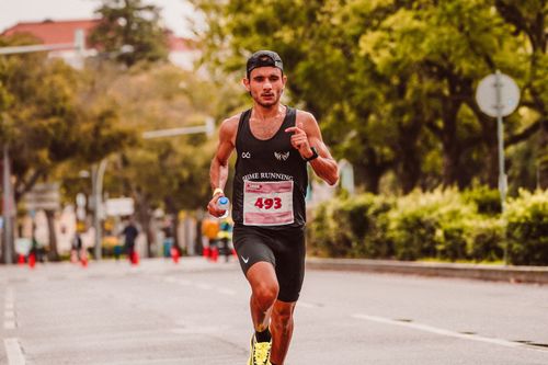 Free Focused male athlete running in a marathon, wearing a tank top and holding a bottle of water. Stock Photo