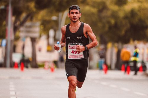 Free Focused male athlete running a marathon with water bottle on city road Stock Photo