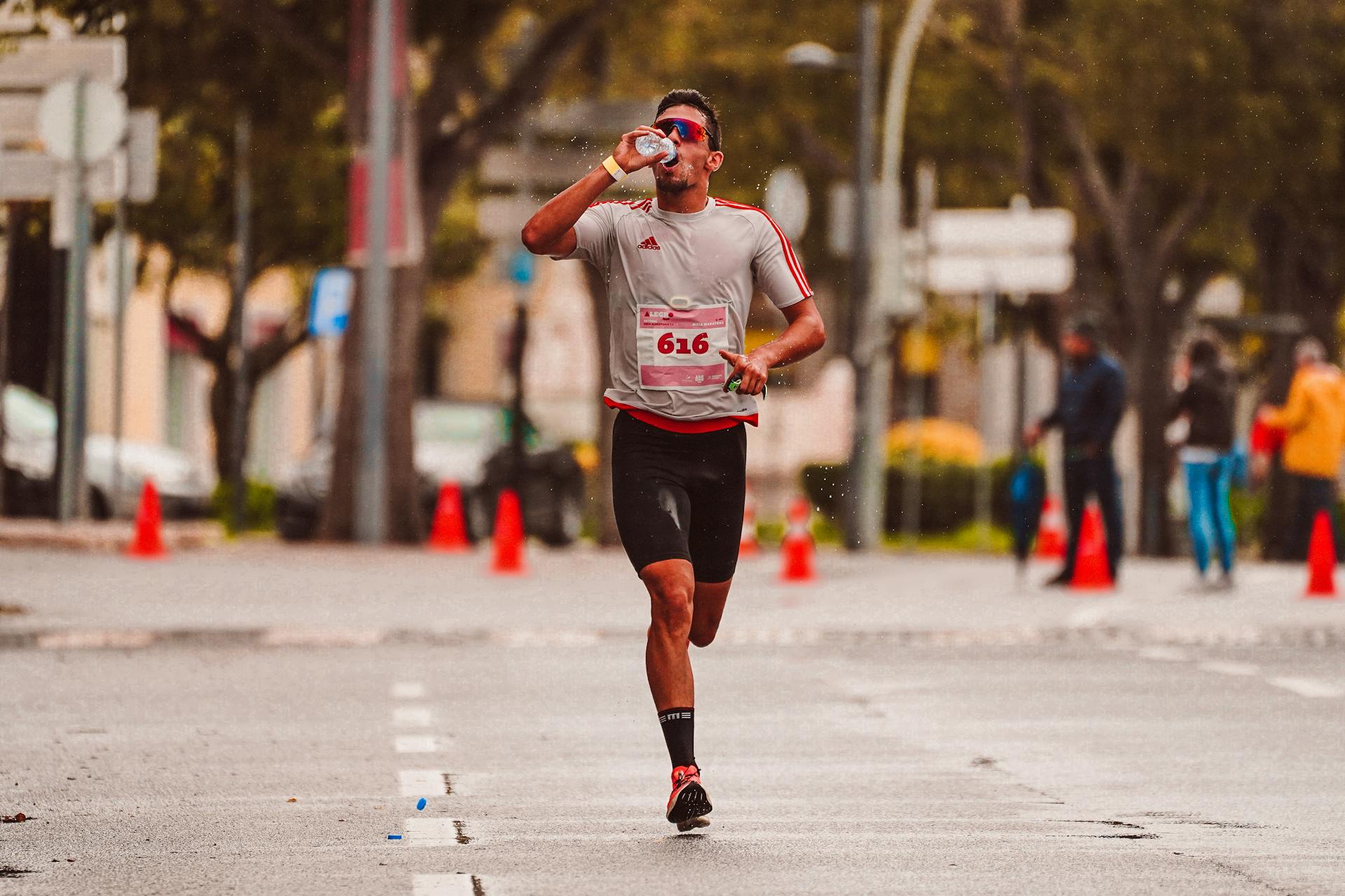 A dedicated runner drinks from a water bottle during a marathon on a city street.