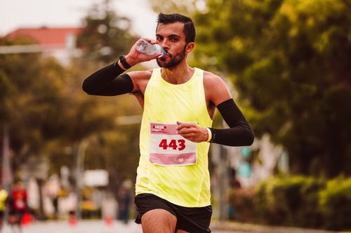 Free Athlete drinking water while running in a marathon. Outdoor exercise. Stock Photo