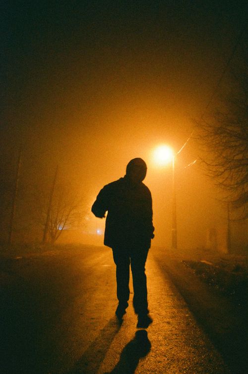 Free A person walking along a foggy street illuminated by a street lamp with a moody atmosphere. Stock Photo