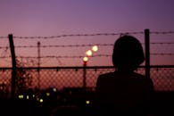 黄昏时分，东京新宿，一名女子的剪影凝视着城市天际线，周围是栅栏和铁丝网