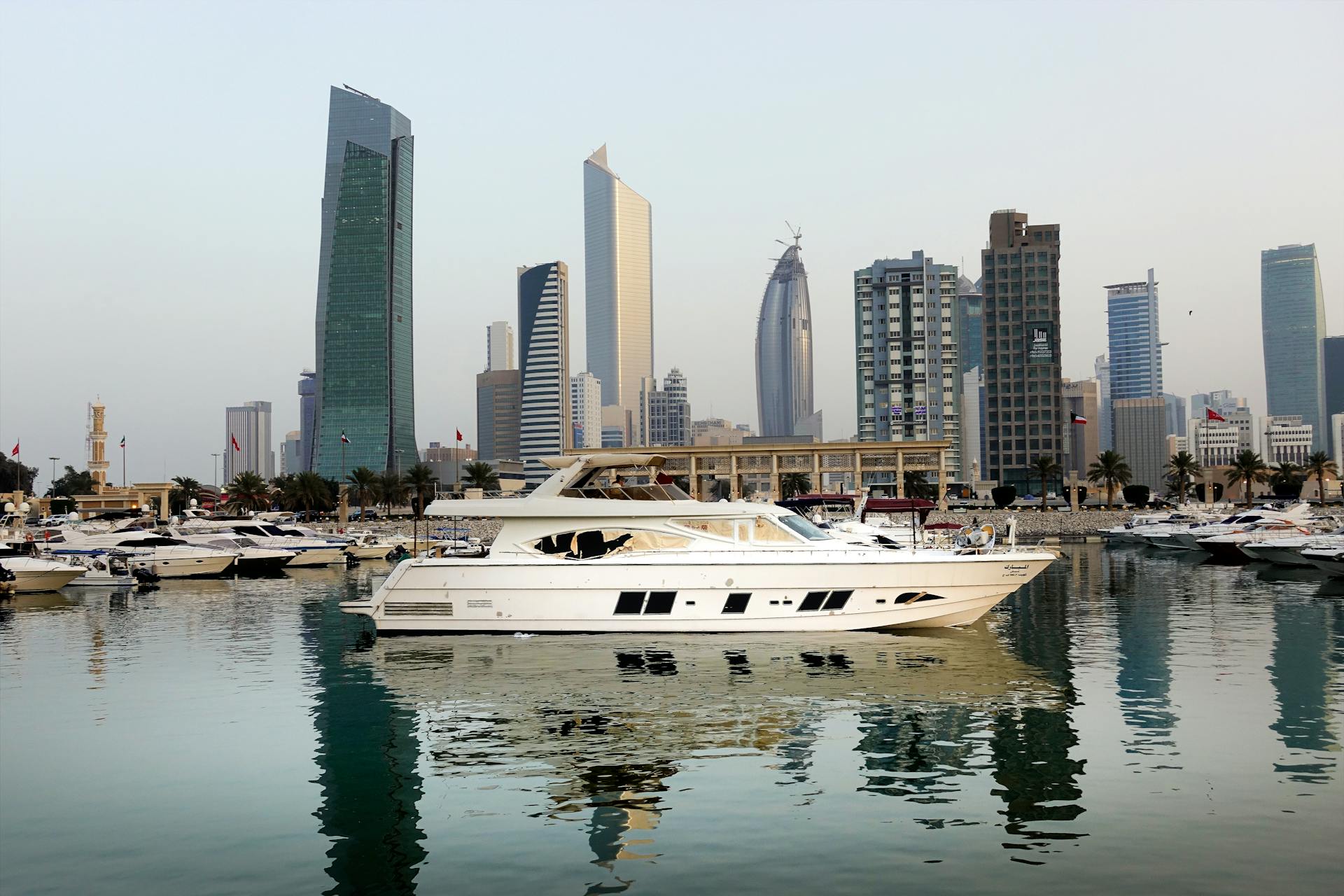 Stunning view of modern skyline in Kuwait City with yachts reflecting on marina waters.