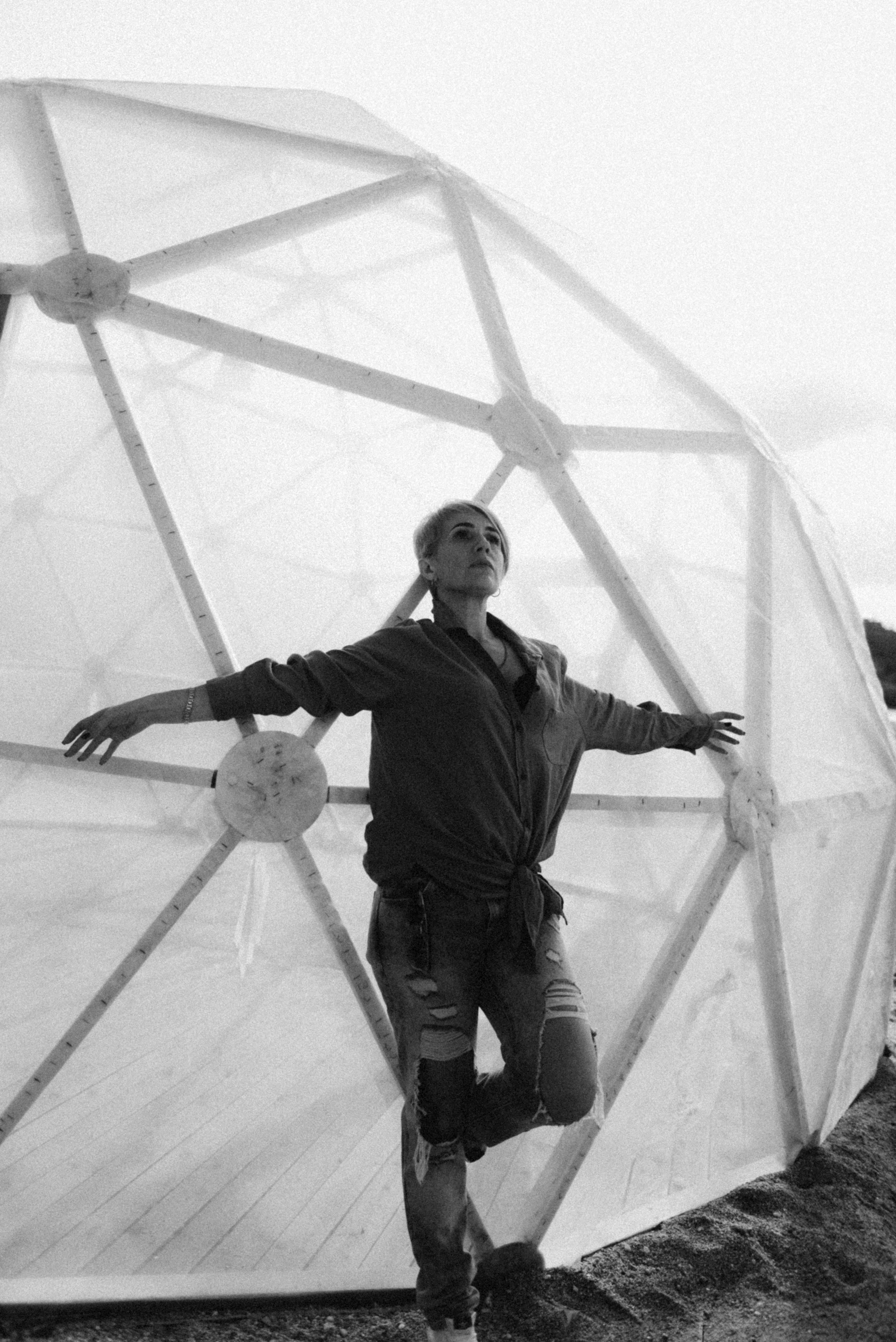 Artistic black and white portrait of a woman posing by a geodesic dome.