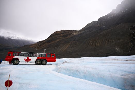 Red Ice Explorer bus on Athabasca Glacier under cloudy sky in Jasper National Park.