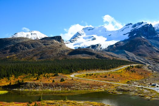 Breathtaking autumn view of Jasper National Park with snow-capped mountains, vibrant foliage, and a winding river.