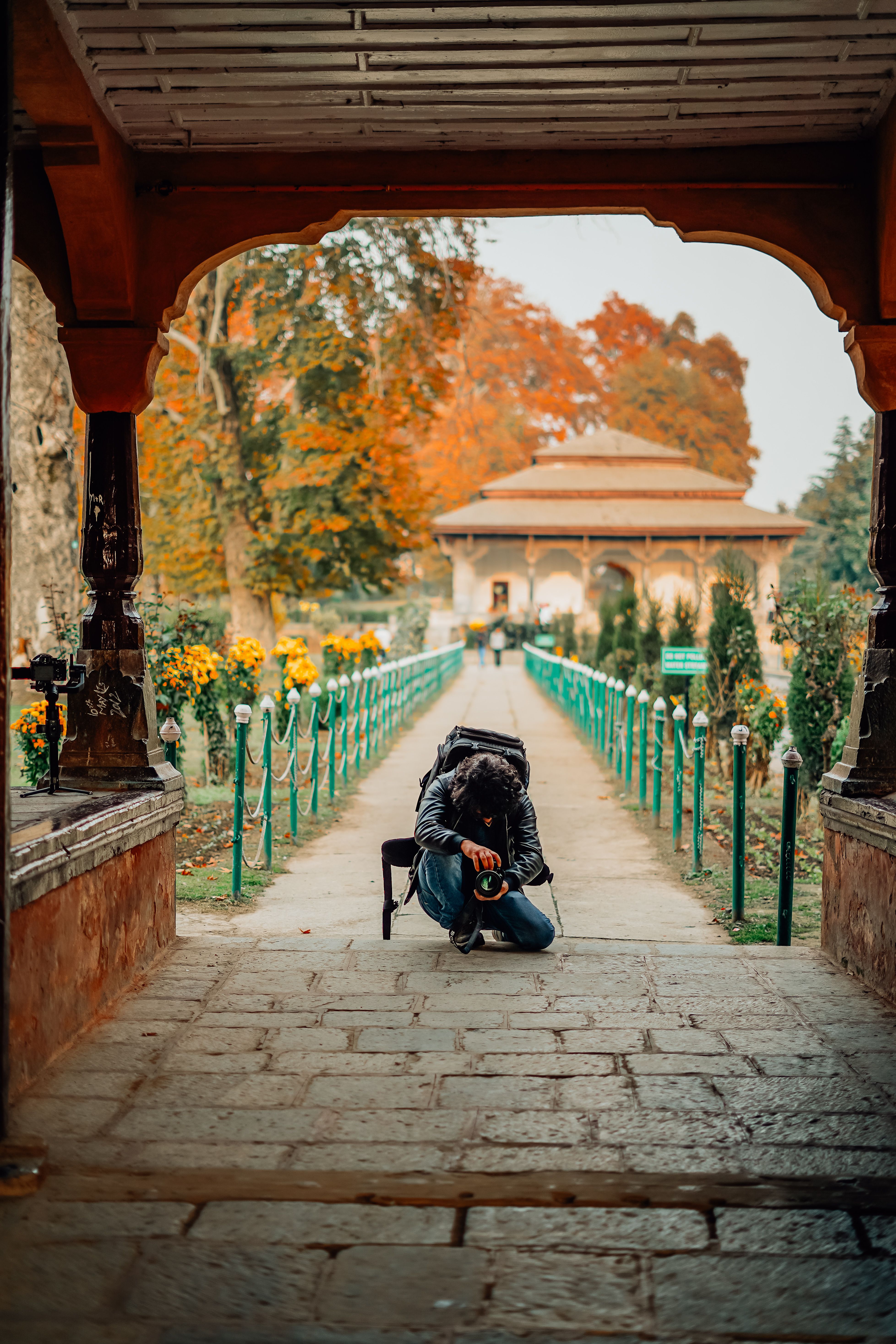 A photographer on a picturesque pathway captures the beauty of autumn foliage with vibrant colors.