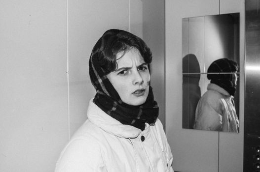Black and white portrait of a woman in an elevator, looking annoyed, with a headscarf and reflection.