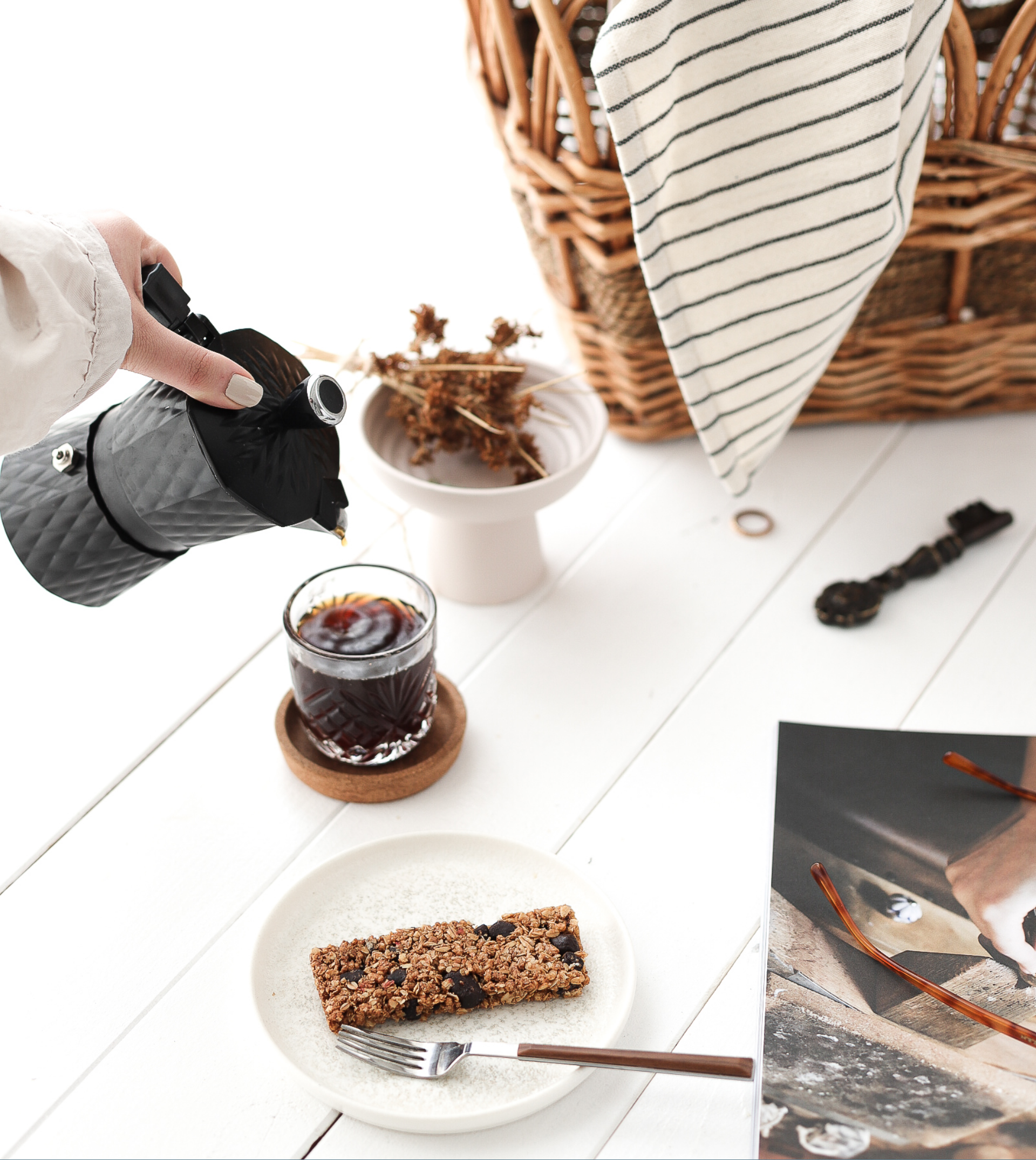 Hand pouring coffee into a cup with a breakfast bar on a white table setting.