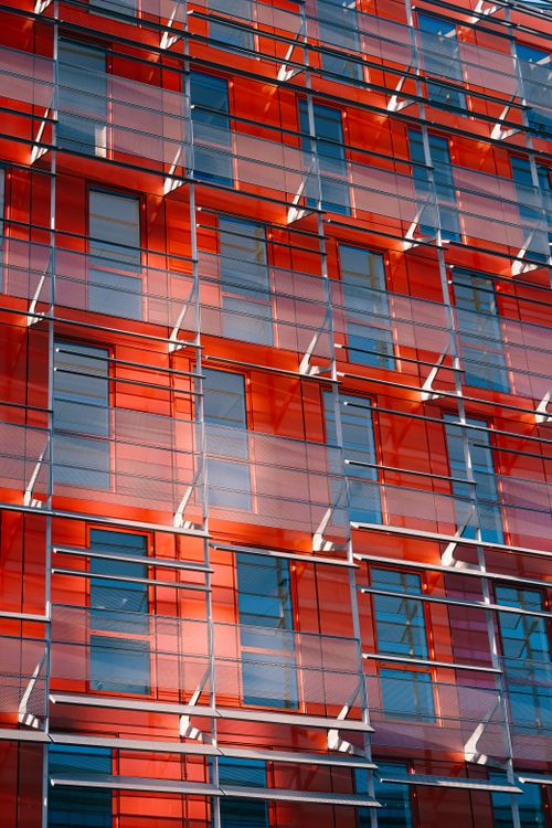 Free Stunning view of a modern building's glass facade with vibrant red panels in urban setting. Stock Photo