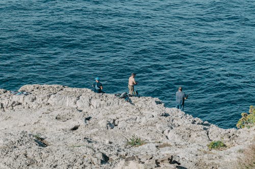 Men Standing on a Rock Formation while Fishing