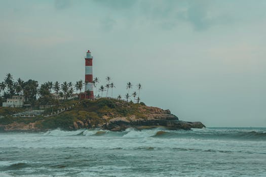 Scenic view of Kovalam Beach lighthouse with palm trees and rocky shore in Kerala, India.