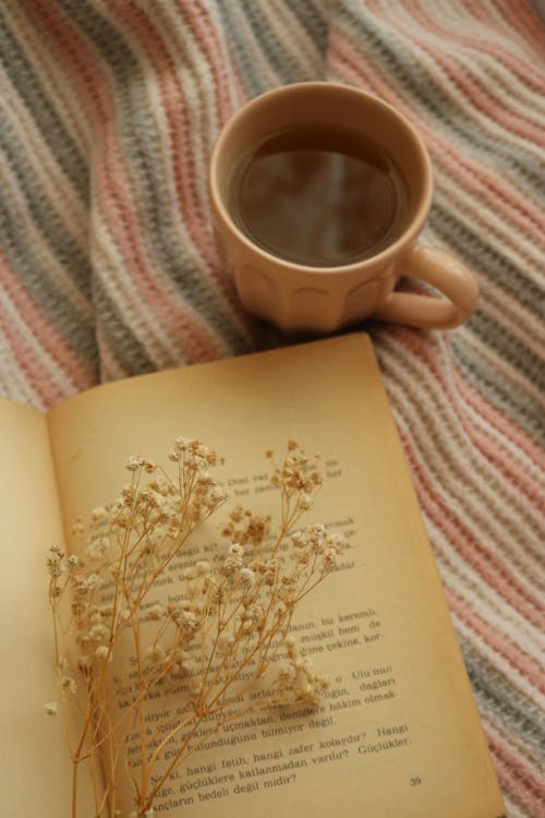 An Open Book with White Flowers Beside a Cup of Coffee