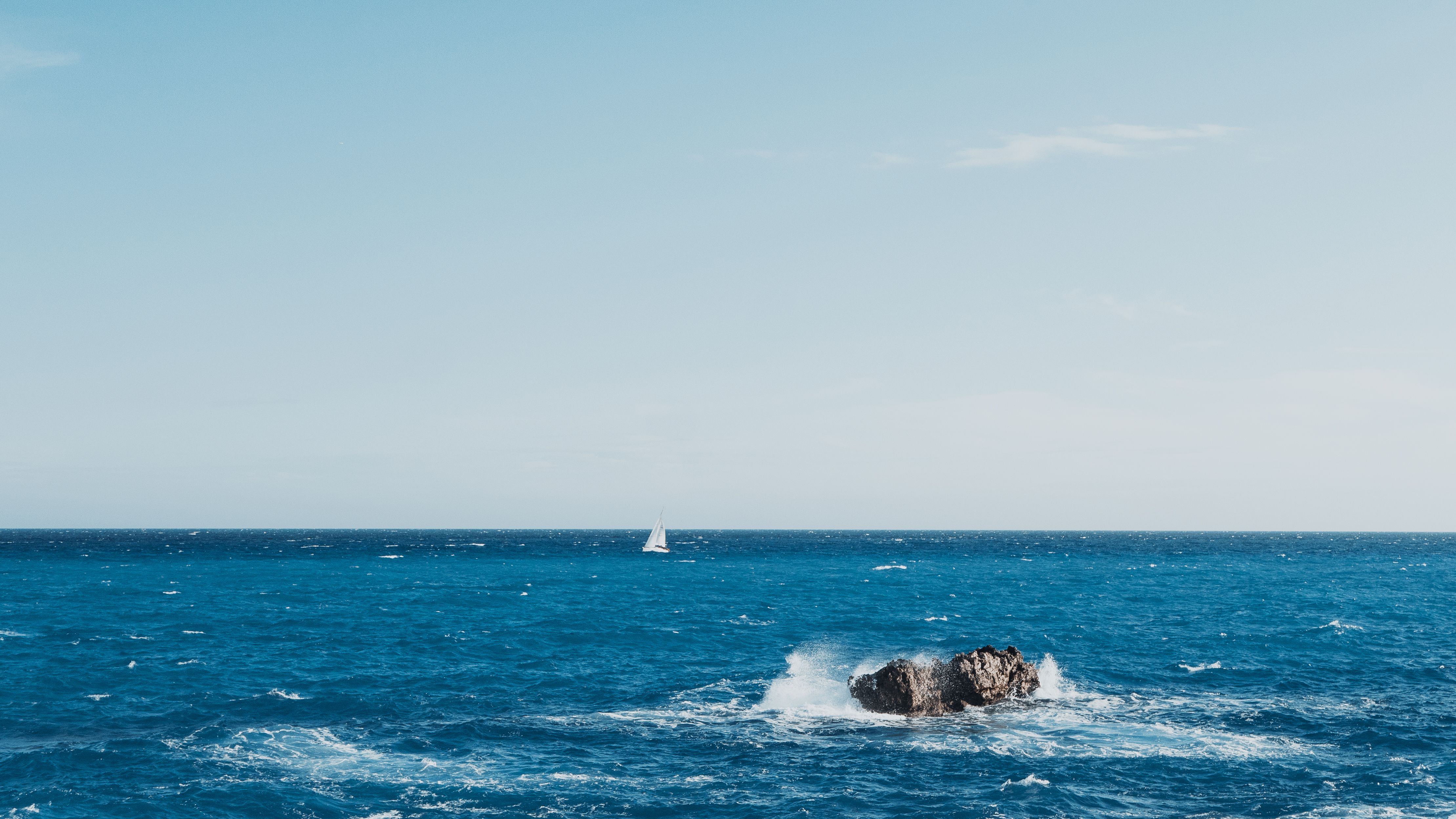 A tranquil ocean view featuring a sailboat and rocky formations under a clear sky.