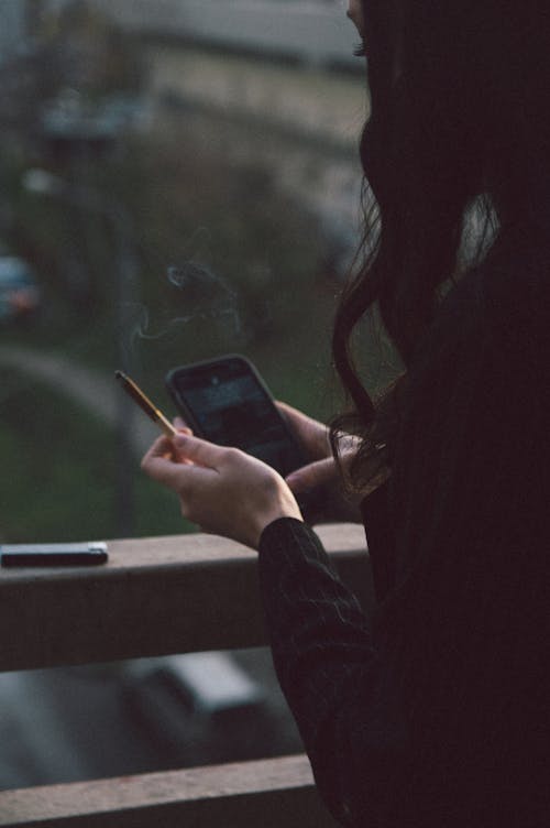 Woman Using Cellphone and Holding a Cigarette