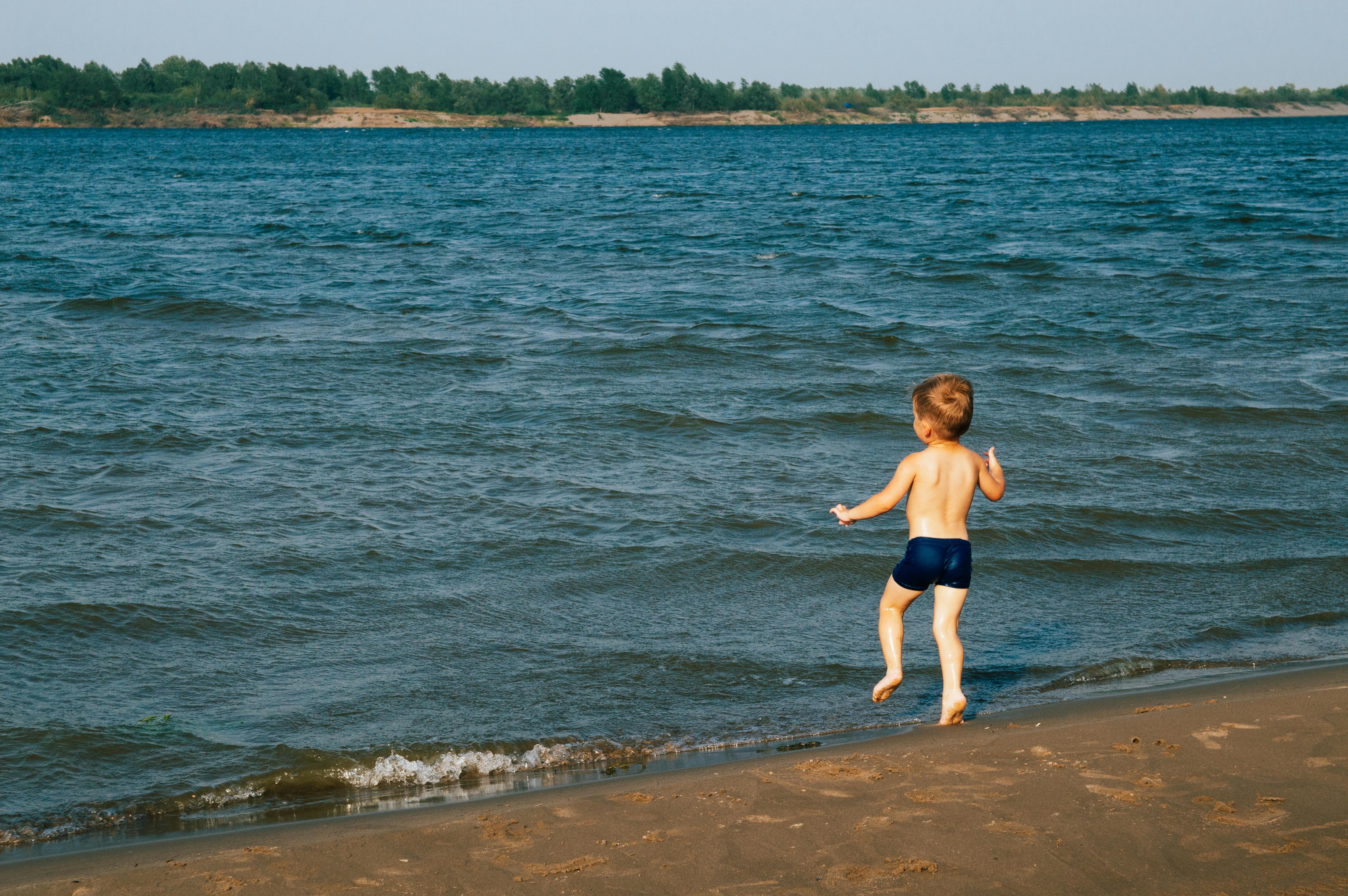 A young boy enjoying the summer at the beach, running barefoot by the water.