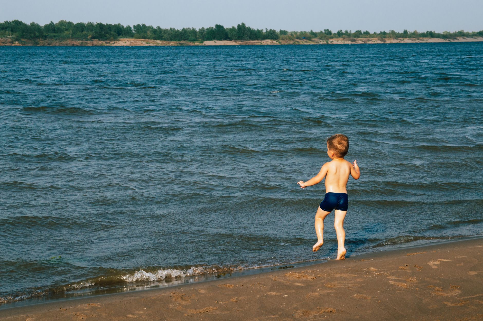 A young boy enjoying the summer at the beach, running barefoot by the water.