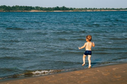 Free A young boy enjoying the summer at the beach, running barefoot by the water. Stock Photo