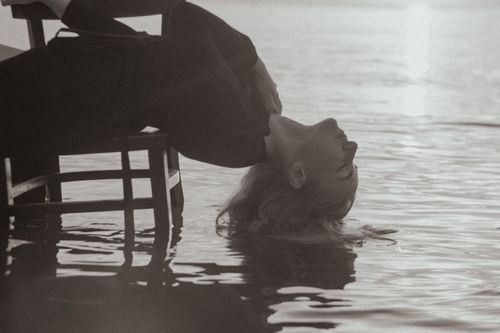 Free A serene black and white portrait of a woman reclining on a chair with hair submerged in water. Stock Photo