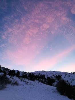 A breathtaking winter sunrise over snow-covered mountains in the French Alps, with pink and blue skies.
