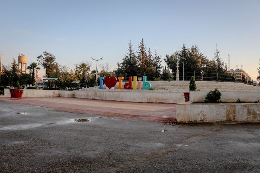 A colorful 'I Love Idlib' sign in a public park in Idlib, Syria, surrounded by trees and clear sky.