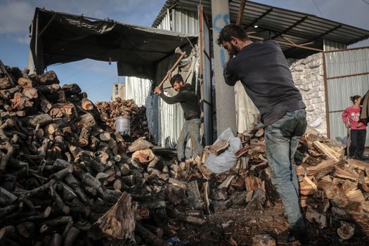 Workers chopping wood in an outdoor setting in Idlib, Syria.