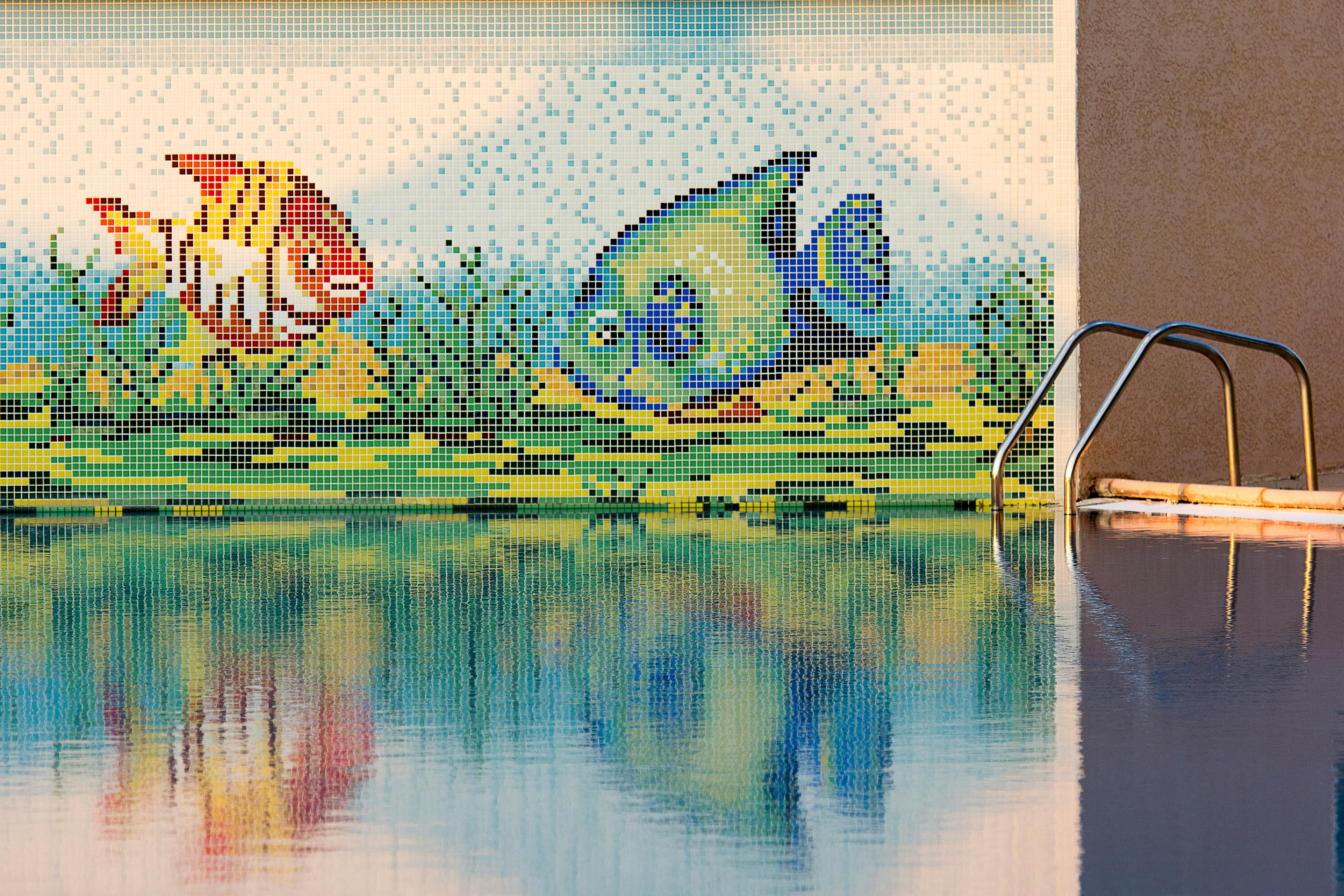 Colorful mosaic fish decor with pool reflection, perfect for summer vibes.