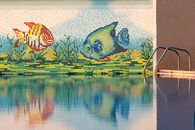 Colorful mosaic fish decor with pool reflection, perfect for summer vibes.