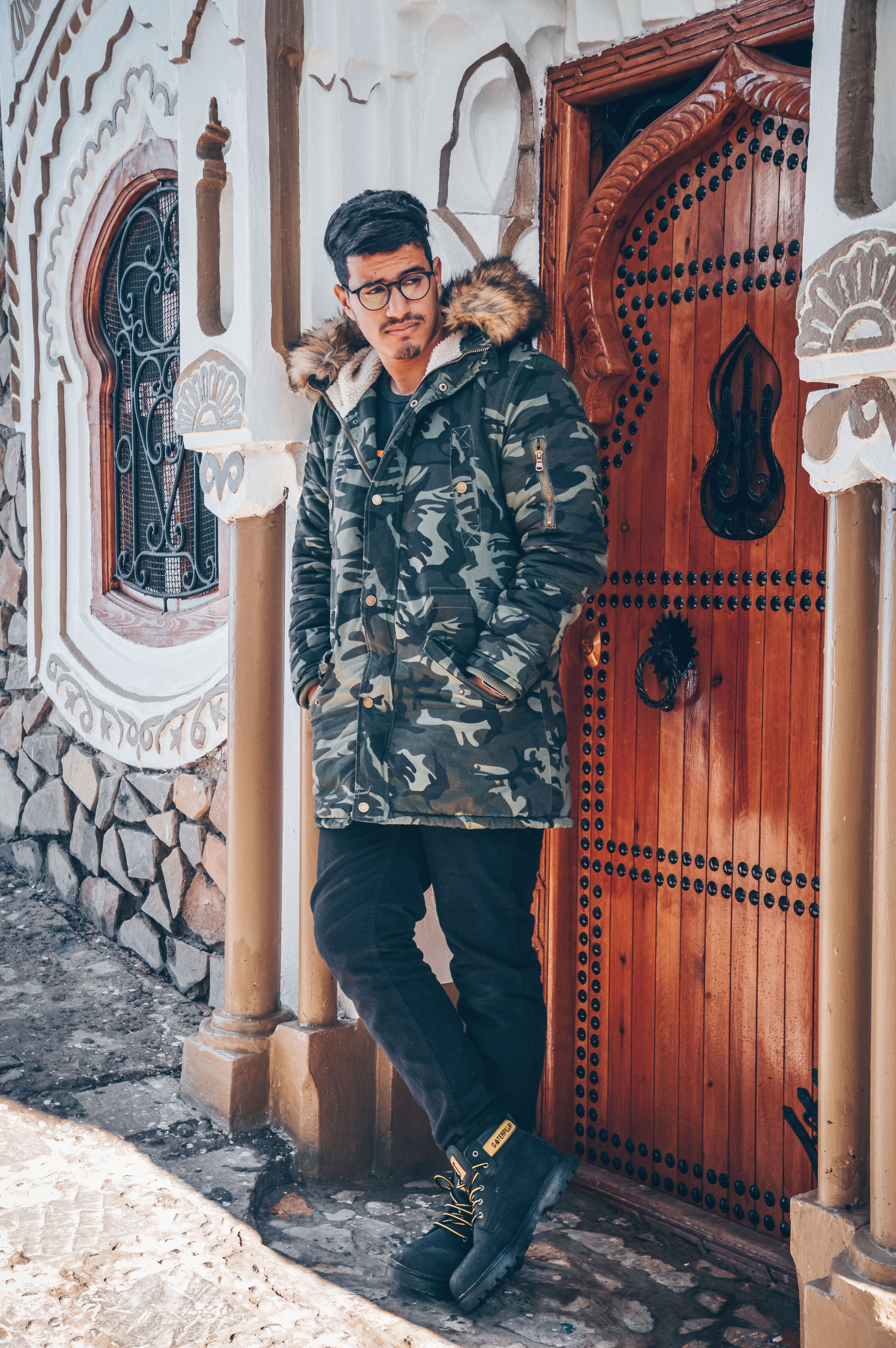Portrait of a man in a camouflage jacket leaning against a colorful door in Chefchaouen, Morocco.